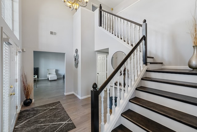 stairs featuring a high ceiling, an inviting chandelier, and wood-type flooring