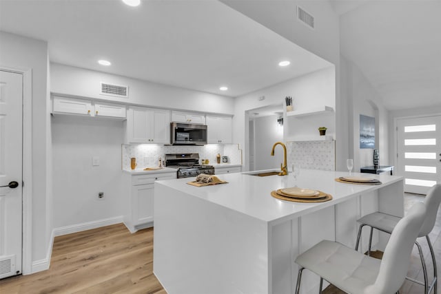 kitchen featuring kitchen peninsula, stainless steel appliances, sink, white cabinets, and light hardwood / wood-style floors