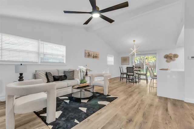 living room with ceiling fan with notable chandelier, light hardwood / wood-style floors, and vaulted ceiling