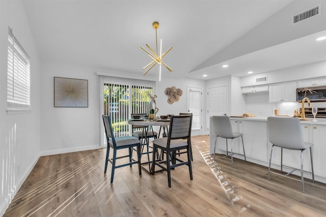 dining space with light hardwood / wood-style floors, an inviting chandelier, and lofted ceiling