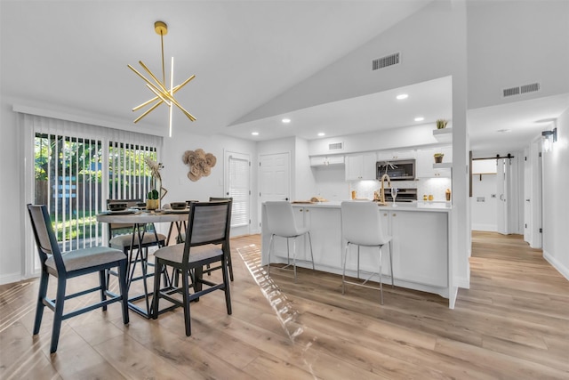 dining area with a barn door, light wood-type flooring, high vaulted ceiling, and a chandelier