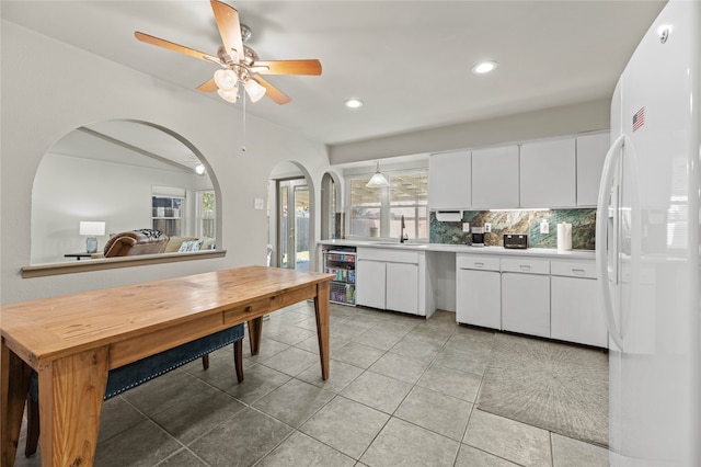 kitchen featuring white refrigerator with ice dispenser, backsplash, sink, white cabinetry, and beverage cooler