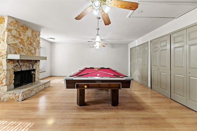 rec room with light wood-type flooring, a stone fireplace, ceiling fan, and pool table