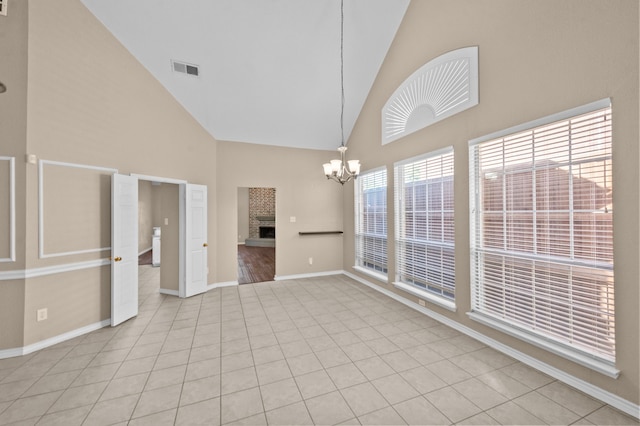 unfurnished living room with a fireplace, high vaulted ceiling, light tile patterned flooring, and an inviting chandelier