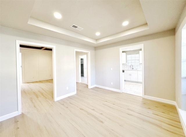 spare room featuring sink, a tray ceiling, and light hardwood / wood-style flooring