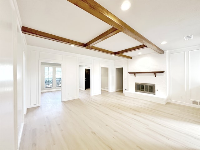 unfurnished living room with beamed ceiling, light hardwood / wood-style floors, and a brick fireplace