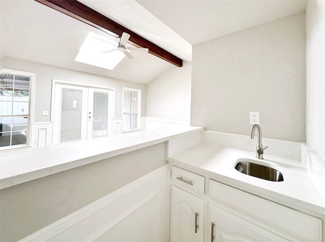 kitchen with white cabinets, vaulted ceiling with skylight, ceiling fan, and sink