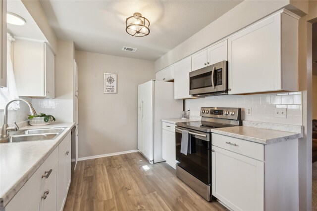 kitchen with decorative backsplash, appliances with stainless steel finishes, sink, white cabinets, and light hardwood / wood-style floors