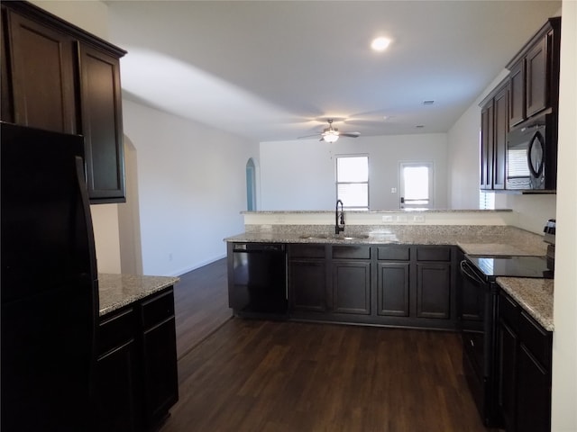 kitchen featuring dark wood-type flooring, black appliances, sink, ceiling fan, and light stone counters