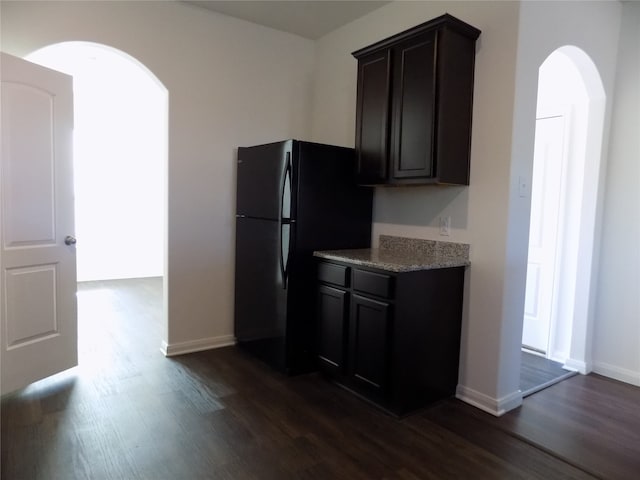 kitchen with black fridge, dark hardwood / wood-style flooring, light stone countertops, and dark brown cabinets