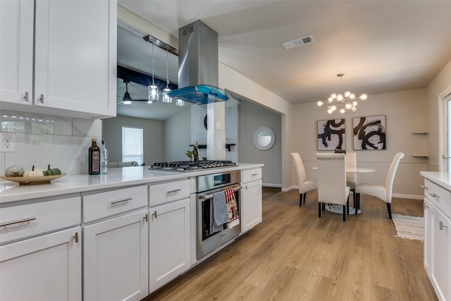 kitchen with pendant lighting, white cabinets, light wood-type flooring, appliances with stainless steel finishes, and island exhaust hood