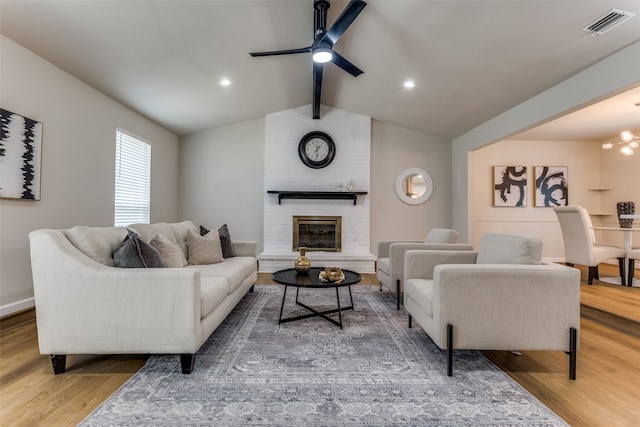 living room with a fireplace, wood-type flooring, lofted ceiling with beams, and ceiling fan with notable chandelier