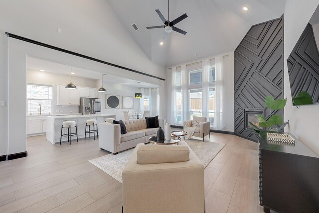 living room featuring high vaulted ceiling, sink, ceiling fan, a fireplace, and light hardwood / wood-style floors