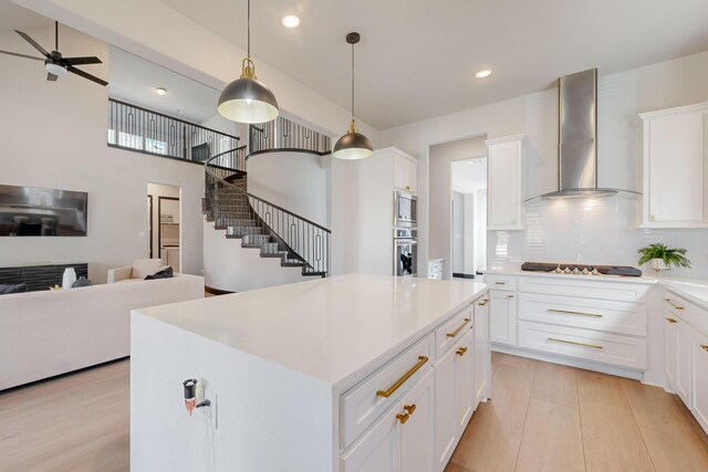 kitchen featuring wall chimney range hood, hanging light fixtures, a kitchen island, white cabinetry, and stainless steel appliances