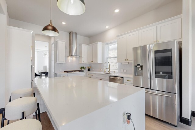 kitchen with pendant lighting, white cabinets, wall chimney exhaust hood, a kitchen island, and stainless steel appliances