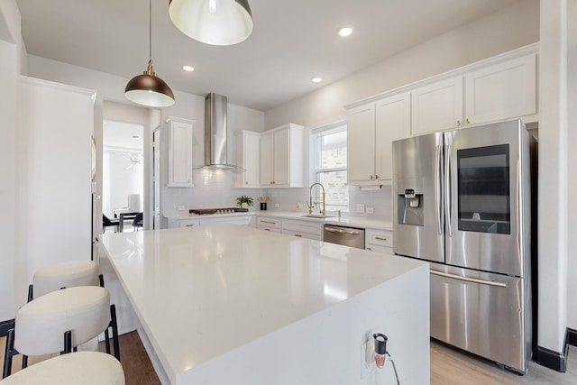 kitchen featuring white cabinetry, appliances with stainless steel finishes, a kitchen island, pendant lighting, and wall chimney range hood