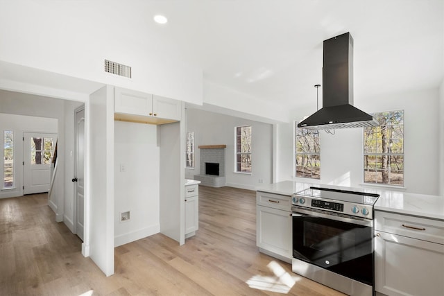 kitchen with stainless steel range with electric cooktop, white cabinetry, pendant lighting, island exhaust hood, and light hardwood / wood-style floors