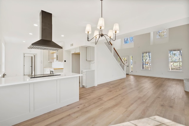 kitchen featuring light wood-type flooring, black electric cooktop, kitchen peninsula, pendant lighting, and island exhaust hood