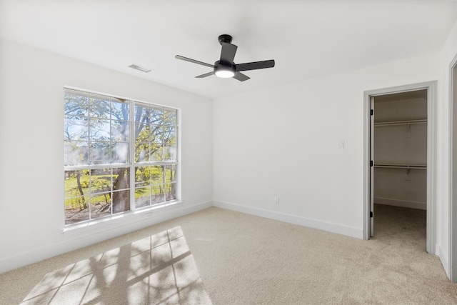 unfurnished bedroom with light carpet, a spacious closet, a closet, and ceiling fan