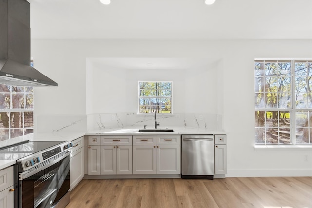 kitchen with appliances with stainless steel finishes, range hood, sink, light stone countertops, and light wood-type flooring