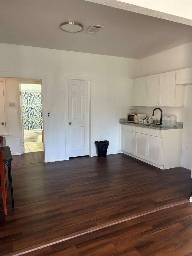 kitchen with white cabinets, dark hardwood / wood-style floors, light stone counters, and sink