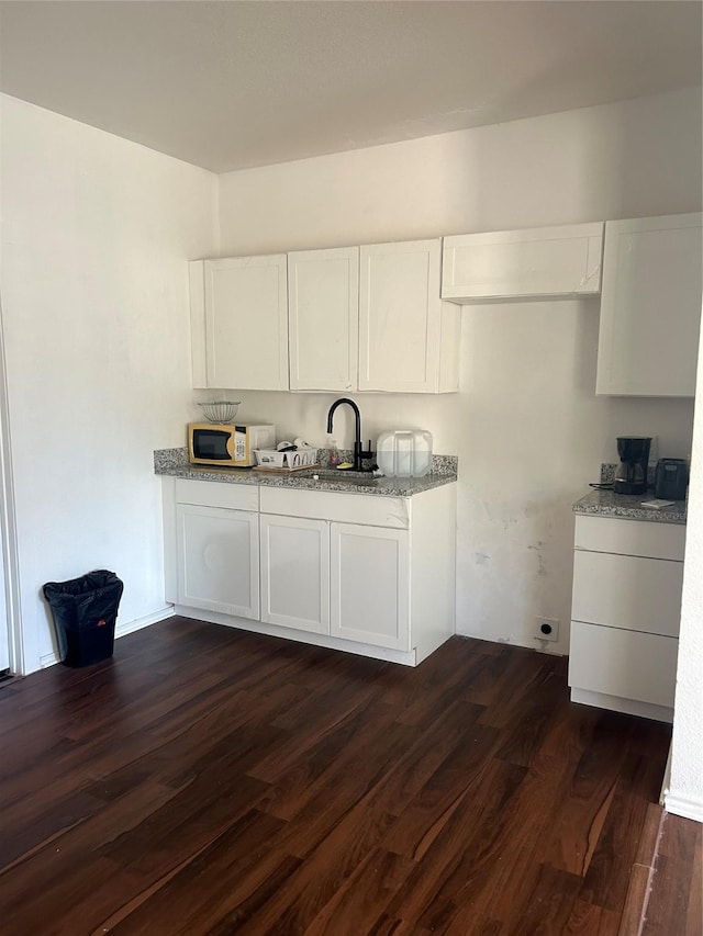 kitchen featuring dark hardwood / wood-style flooring, light stone counters, white cabinetry, and sink