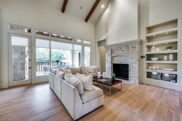 living room featuring built in shelves, beam ceiling, high vaulted ceiling, light hardwood / wood-style flooring, and a fireplace