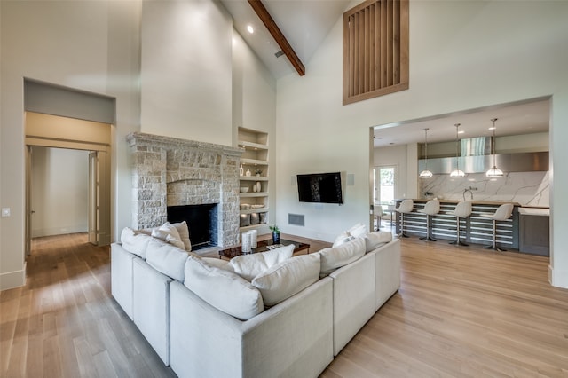 living room featuring high vaulted ceiling, light hardwood / wood-style flooring, built in shelves, a fireplace, and beamed ceiling