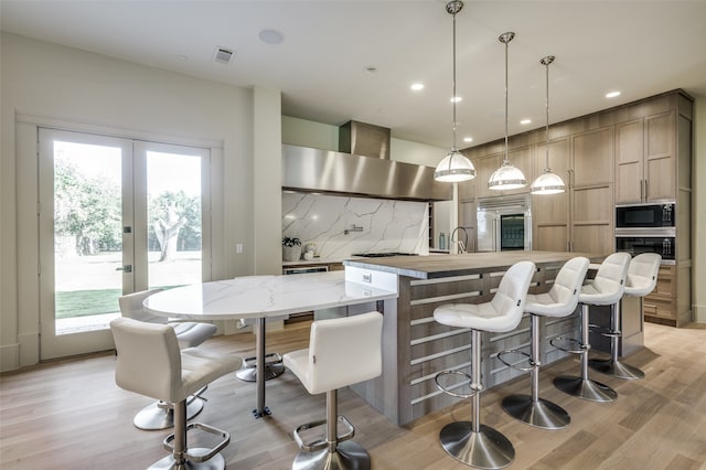 kitchen featuring black appliances, decorative light fixtures, wall chimney range hood, and a wealth of natural light