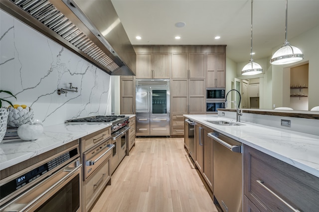 kitchen with dishwasher, wall chimney exhaust hood, sink, light stone counters, and pendant lighting