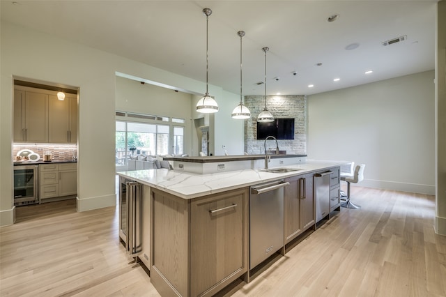 kitchen featuring a large island with sink, sink, light stone countertops, light hardwood / wood-style floors, and beverage cooler