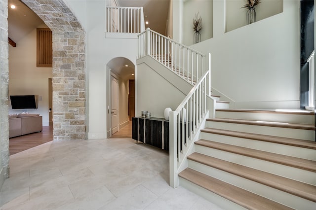 staircase with wood-type flooring and a towering ceiling