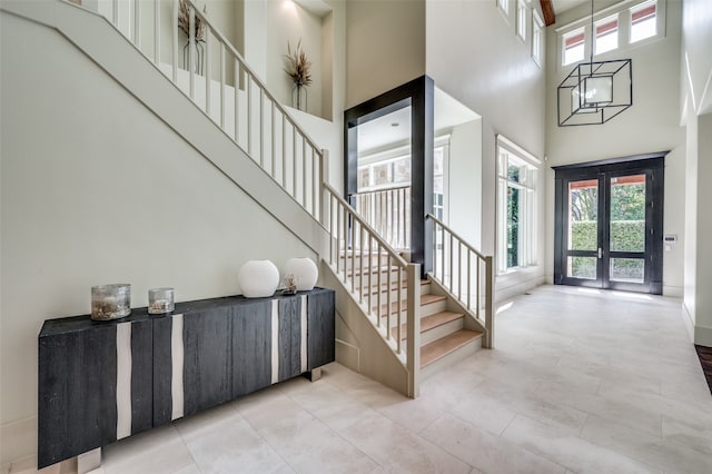 entrance foyer with a notable chandelier, a healthy amount of sunlight, a towering ceiling, and french doors