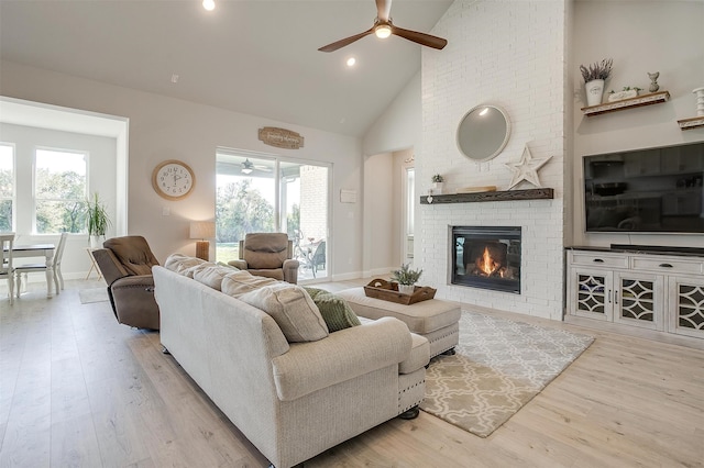 living room with a brick fireplace, light wood-type flooring, high vaulted ceiling, and a healthy amount of sunlight