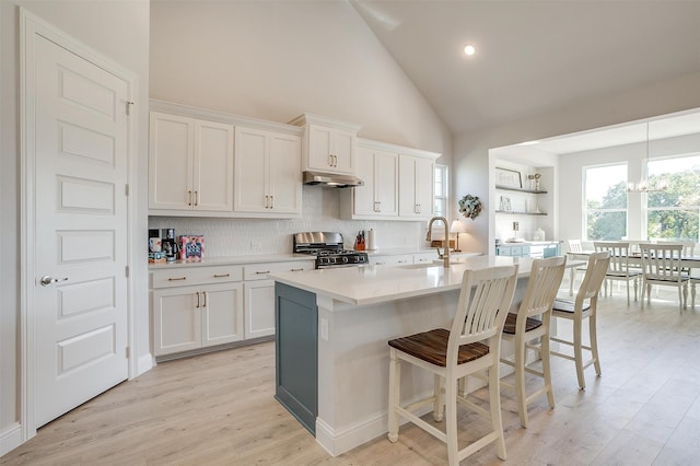 kitchen with stainless steel gas stove, high vaulted ceiling, white cabinetry, and sink