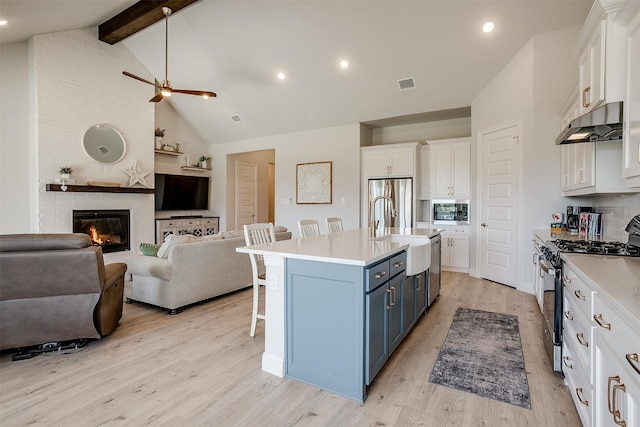 kitchen featuring blue cabinetry, stainless steel appliances, a kitchen island with sink, a breakfast bar, and white cabinets