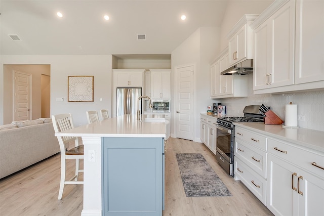 kitchen with a breakfast bar, stainless steel appliances, sink, light hardwood / wood-style floors, and an island with sink