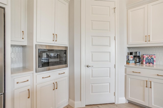 kitchen with tasteful backsplash, white cabinetry, and light wood-type flooring