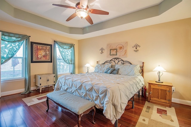 bedroom with ceiling fan, hardwood / wood-style floors, multiple windows, and a tray ceiling