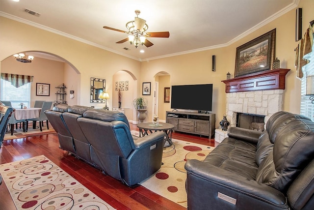 living room featuring ceiling fan, dark hardwood / wood-style flooring, ornamental molding, and a stone fireplace