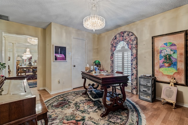 home office with a notable chandelier, light wood-type flooring, a textured ceiling, and ornate columns