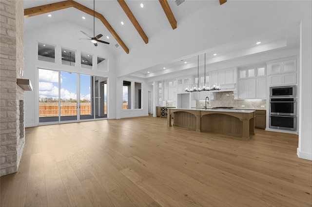 unfurnished living room featuring beam ceiling, ceiling fan, light hardwood / wood-style flooring, high vaulted ceiling, and a fireplace