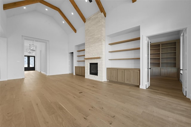 unfurnished living room featuring high vaulted ceiling, a stone fireplace, built in features, beam ceiling, and light hardwood / wood-style floors