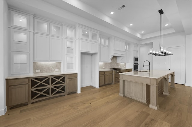 kitchen with light hardwood / wood-style flooring, pendant lighting, a center island with sink, white cabinets, and appliances with stainless steel finishes