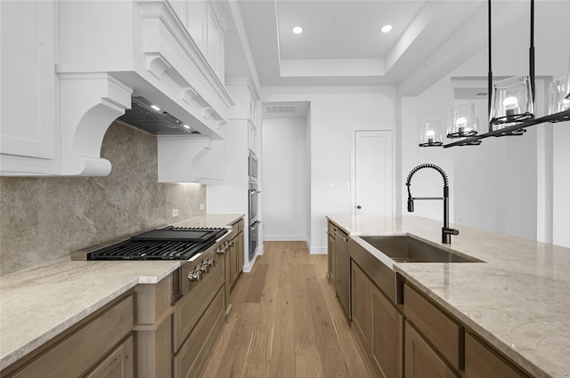 kitchen with white cabinetry, sink, light stone counters, and decorative light fixtures