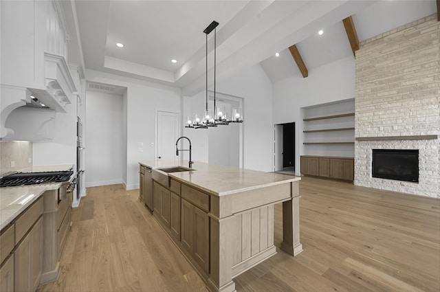 kitchen featuring pendant lighting, a stone fireplace, sink, light stone countertops, and an island with sink