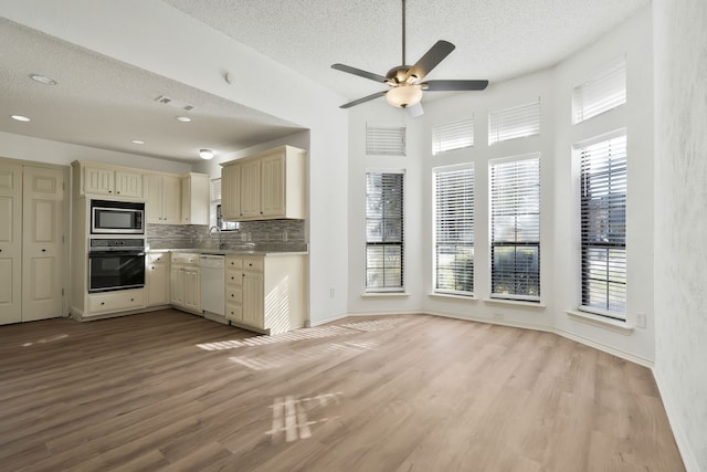 kitchen with backsplash, black oven, stainless steel microwave, and light wood-type flooring