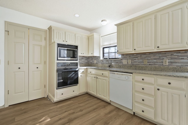 kitchen featuring white dishwasher, sink, cream cabinetry, black oven, and stainless steel microwave