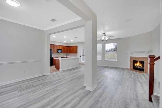 unfurnished living room featuring ornamental molding, ceiling fan, sink, a tile fireplace, and light hardwood / wood-style flooring