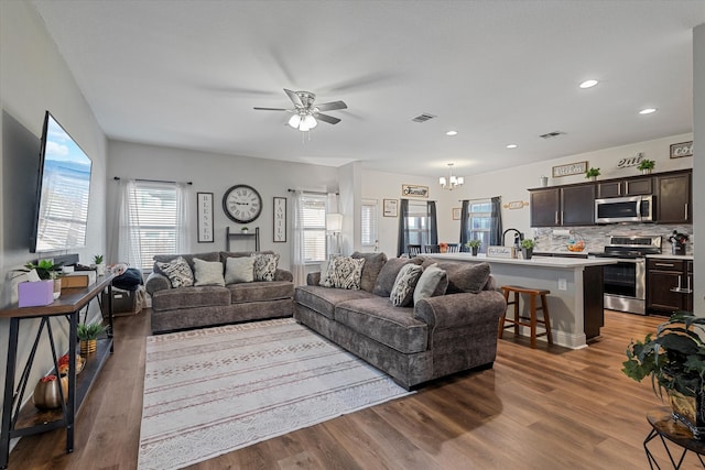 living room with hardwood / wood-style flooring, ceiling fan with notable chandelier, and sink